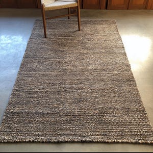 Textured wool rug with dense woven pattern in warm neutrals, modern minimalist home décor floor rug under wooden chair.