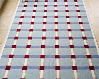 May include: A rectangular area rug featuring a light blue background with a grid pattern composed of intersecting white vertical and horizontal lines, accented by small, solid red squares at each intersection point across the entire surface.
