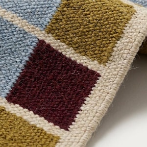 Close-up of the flatweave wool texture showing the tight reversible weave, flat no-pile surface and the interlocked yarns that form each colored square.