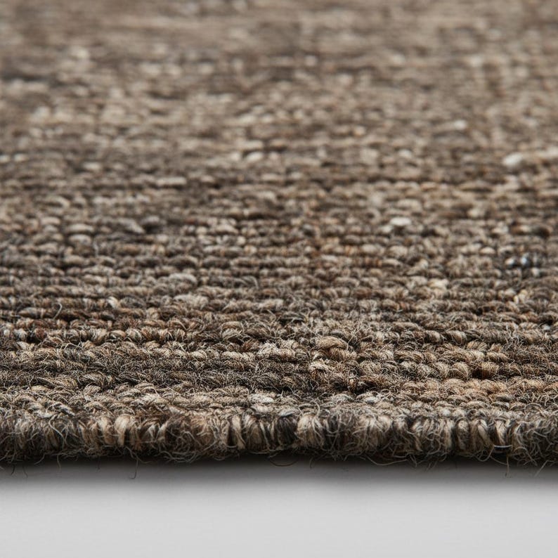 Chunk wool rug with thick handwoven texture in neutral tones placed on concrete floor, modern farmhouse style area rug for living room décor.