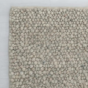 Puede incluir: Primer plano de una alfombra texturizada de color gris claro. La superficie de la alfombra está cubierta de pequeñas texturas redondeadas y nudosas, creando un patrón táctil y visualmente interesante. La paleta de colores es neutra, con variaciones de gris y beige.