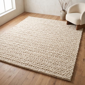 May include: A large, rectangular area rug featuring a chunky, cable-knit texture in a solid cream color. The rug is constructed from thick, braided yarn strands that create a repeating, uniform pattern across the entire surface of the floor covering.