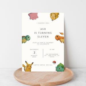 May include: A cream-colored birthday invitation featuring various cartoon characters. The invitation reads "Ash is turning eleven" with event details. The design includes a wooden tray and the text "Gotta Catch 'Em All".