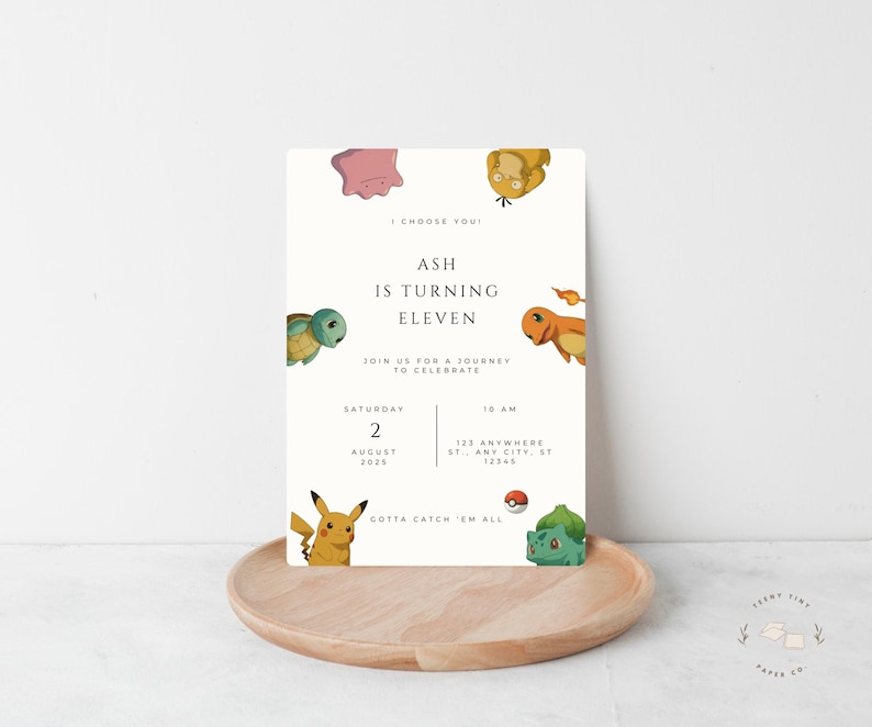 May include: A cream-colored birthday invitation featuring various cartoon characters. The invitation reads "Ash is turning eleven" with event details. The design includes a wooden tray and the text "Gotta Catch 'Em All".
