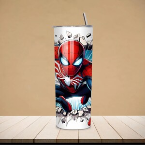 May include: A white 20 oz tumbler featuring a vibrant illustration of Spider-Man breaking through a wall. The design showcases Spider-Man in his classic red and blue suit, with a silver straw and lid.