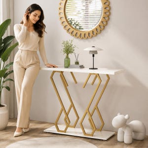 May include: A white console table featuring a rectangular top and a base constructed from gold-coloured metal with geometric, angular shapes. The table stands on a flat white rectangular platform base, providing a stable foundation for the structure.