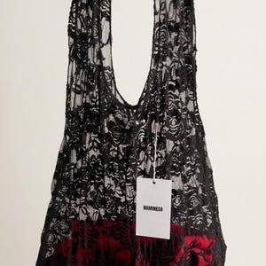 Può includere: Borsa tote in pizzo nero con motivo a rose, tenuta in mano. La borsa ha una fodera rossa visibile sul fondo e un'etichetta con la scritta "NAMINESO".
