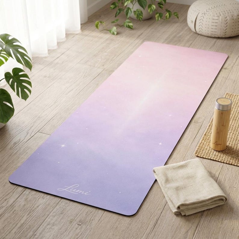 May include: A yoga mat with a gradient design, transitioning from lavender to pink. The mat features a subtle star pattern and the word "Lumi" in cursive. A bamboo water bottle and a folded beige towel are next to the mat.