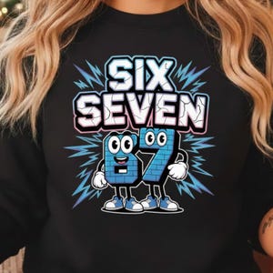 以下が含まれることがあります： ひび割れたアウトラインフォントで「SIX SEVEN」という言葉が書かれた黒いスウェットシャツ。 下には、目、腕、脚で擬人化された数字「67」があり、稲妻のグラフィックに囲まれています。 数字は青と白です。