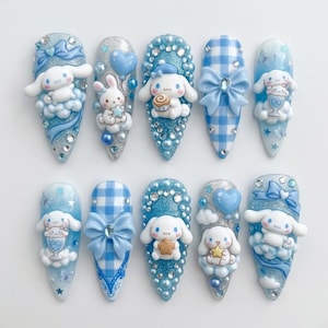 May include: A set of ten press-on nails featuring light blue and white color schemes. The designs include 3D figures of white puppies, blue bows, gingham patterns, glitter, rhinestones, clouds, stars, and small dessert-themed charms.