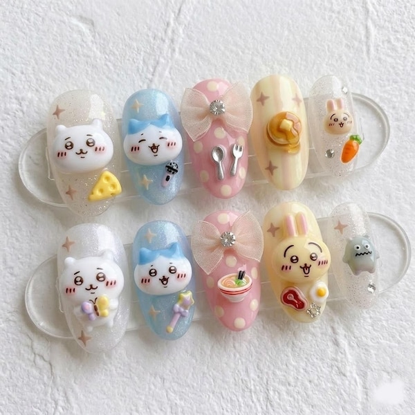 May include: A set of ten press-on nails featuring 3D charms including white cat faces, pink bows, a pancake stack, a carrot, a bowl of ramen, a fried egg, a piece of meat, and a small gray monster, all decorated with glitter and star accents.