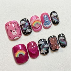 Peut inclure: Dix faux ongles avec divers motifs. Les ongles présentent des personnages de Care Bears, des arcs-en-ciel, des cœurs, des nuages et un thème galactique. Les couleurs incluent le rose, le bleu, le noir et des paillettes irisées.
