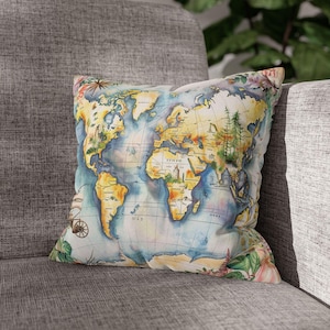 Può includere: Un cuscino decorativo con un design a mappa del mondo ad acquerello. La mappa, nei toni del blu, giallo e verde, è su uno sfondo bianco. Motivi floreali decorano i bordi del cuscino, aggiungendo un elemento naturale al design.