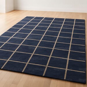 May include: A navy blue rug featuring a grid pattern in a lighter beige hue. The rectangular rug is placed on a light wooden floor. The grid design is evenly distributed across the rug's surface.