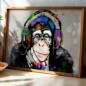 May include: A framed print of a chimpanzee wearing headphones with a colourful design. The chimpanzee's face is detailed with a light pink muzzle and expressive eyes. Splashes of paint in various colours surround the subject, creating a vibrant and modern aesthetic.