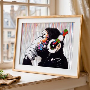 May include: A framed art print showing a chimpanzee wearing headphones. The image is in black and white, with colourful accents on the chimpanzee's face and headphones. The background features vertical lines of various colours.
