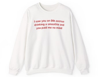 May include: A white long-sleeve crewneck sweatshirt featuring red text printed on the chest that reads: I saw you on 8th avenue drinking a smoothie and you paid me no mind. The garment has a ribbed collar, cuffs, and a straight hemline.