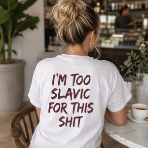 May include: A white short-sleeved t-shirt featuring dark maroon text printed on the back. The text reads, I'M TOO SLAVIC FOR THIS SHIT, written in a bold, slightly distressed, brush-stroke style font. The shirt has a crew neckline and short sleeves.