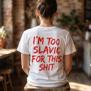 以下が含まれることがあります： 背面に赤い文字で「I'M TOO SLAVIC FOR THIS SHIT」とプリントされた白い半袖Tシャツ。文字は太い筆致のスタイルで書かれています。Tシャツはクルーネックで標準的なフィット感があり、背面から見た様子です。