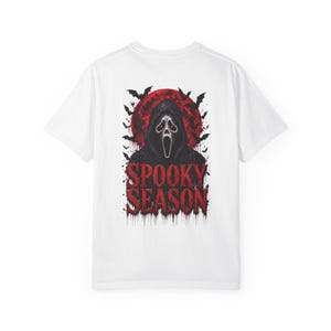 以下が含まれることがあります： 背面にグラフィックがプリントされた白い半袖Tシャツ。白いマスクを被ったフード付きの人物、大きな赤い月、黒いコウモリが描かれています。人物の下には、赤い滴るようなフォントで「SPOOKY SEASON」という文字がプリントされています。