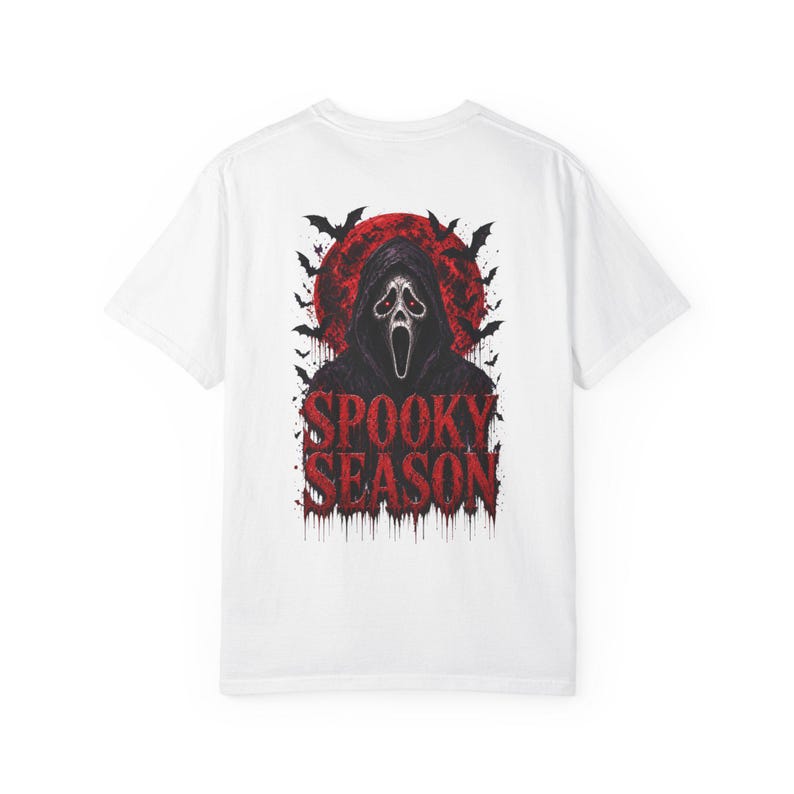 以下が含まれることがあります： 背面にグラフィックがプリントされた白い半袖Tシャツ。白いマスクを被ったフード付きの人物、大きな赤い月、黒いコウモリが描かれています。人物の下には、赤い滴るようなフォントで「SPOOKY SEASON」という文字がプリントされています。