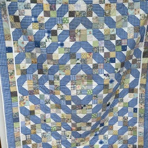 May include: A patchwork quilt with a blue and white gingham pattern. The quilt features squares of floral and solid fabrics in shades of blue, white, green, yellow, and brown. The border is a blue and white gingham. A handmade item.