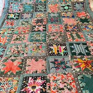 May include: A patchwork quilt featuring a repeating star block pattern constructed from various colourful floral, geometric, and polka dot fabric squares. The quilt is bordered by a light blue fabric with white polka dots and dark grey sashing.
