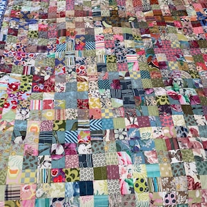May include: A colourful patchwork quilt composed of numerous fabric squares. The quilt showcases a variety of patterns, including florals and geometric shapes, in shades of pink, blue, green, and brown. It has a blue border.