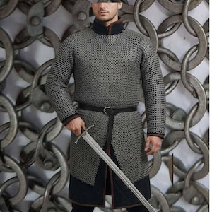 May include: A silver chainmail shirt with long sleeves, a black collar, and a black belt. The shirt extends to the mid-thigh and is paired with black pants. A silver sword is held in the right hand. The background features a chain design.