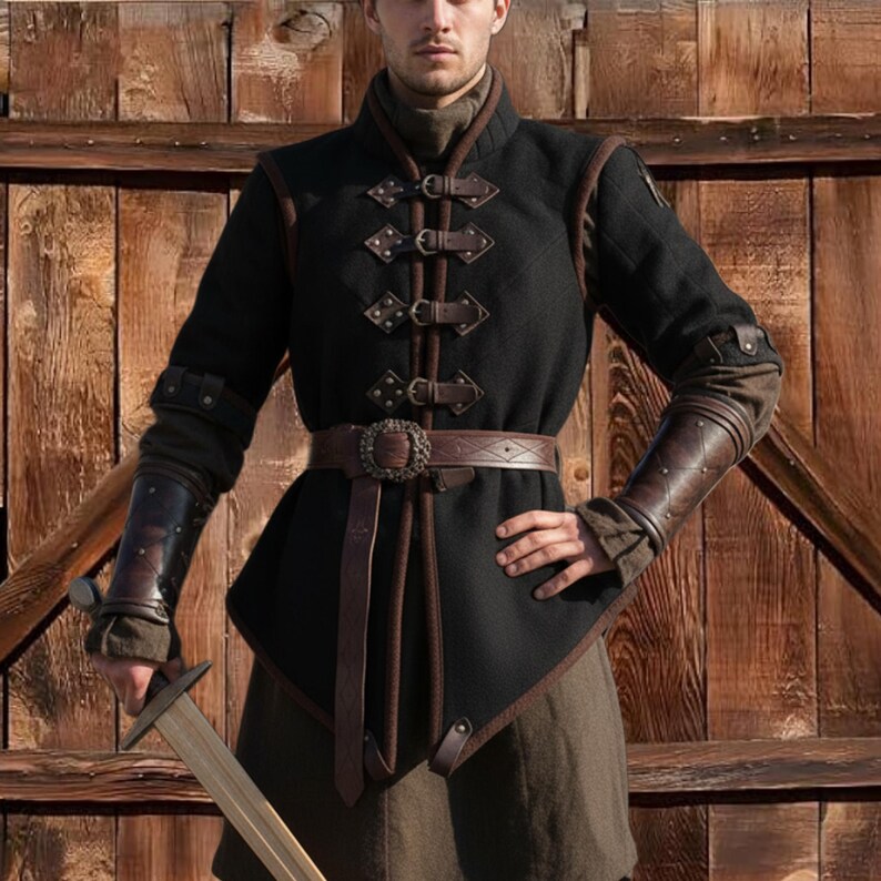 May include: Black medieval-style tunic with brown leather accents, including a belt and arm guards. The tunic features decorative clasps and a high collar. The outfit is designed for historical reenactment or costume use.