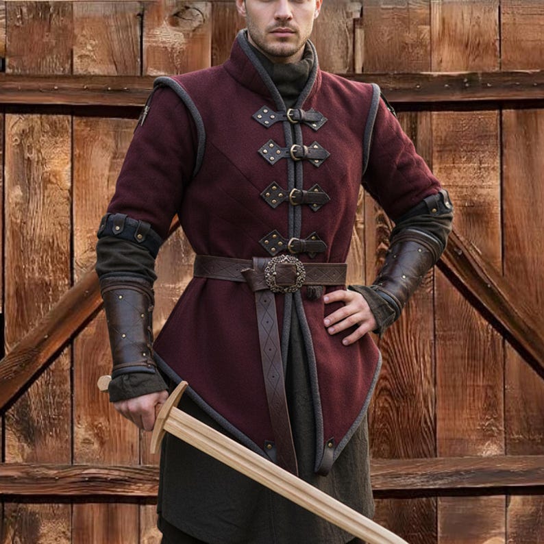 May include: Burgundy medieval-style tunic with a high collar, leather accents, and decorative buckles. The tunic features a brown leather belt with a detailed buckle and is paired with matching arm guards. A wooden sword is held in the hand.