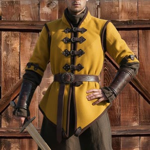May include: Mustard yellow medieval-style tunic with brown leather accents and a matching belt. The tunic features decorative clasps and leather arm guards. The outfit is reminiscent of historical attire.