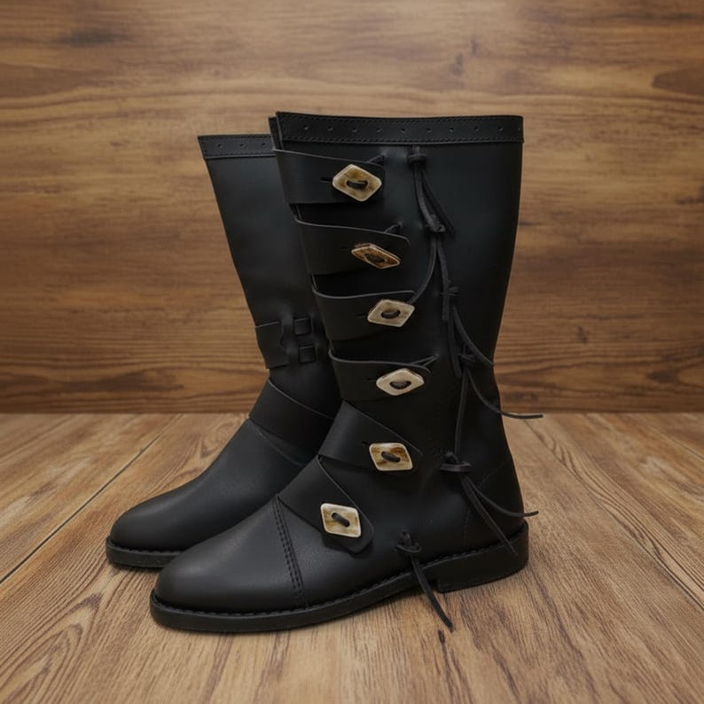 May include: A pair of black leather boots with multiple straps and decorative buttons. The boots have a knee-high design and are set against a wooden background. The boots have a classic, timeless style.