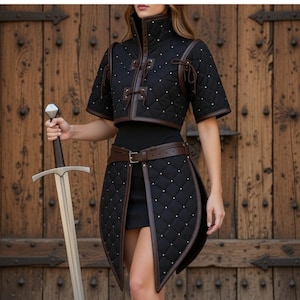 May include: Black quilted medieval-style outfit with brown leather trim and accents. The outfit includes a cropped jacket, a skirt with a split front, and a belt. The outfit is adorned with small white studs. A silver sword is held in the hand.