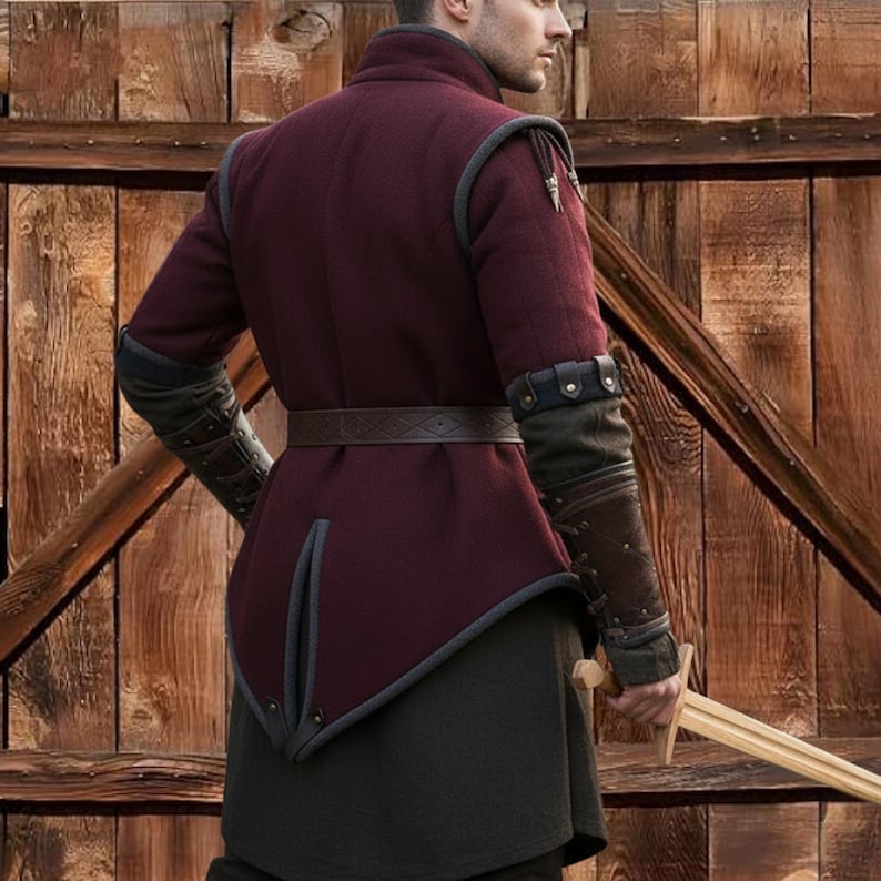 May include: A burgundy medieval-style jacket with gray trim and a brown leather belt. The jacket has long sleeves with dark gray and brown accents. The person is holding a wooden sword. The background is a wooden door.