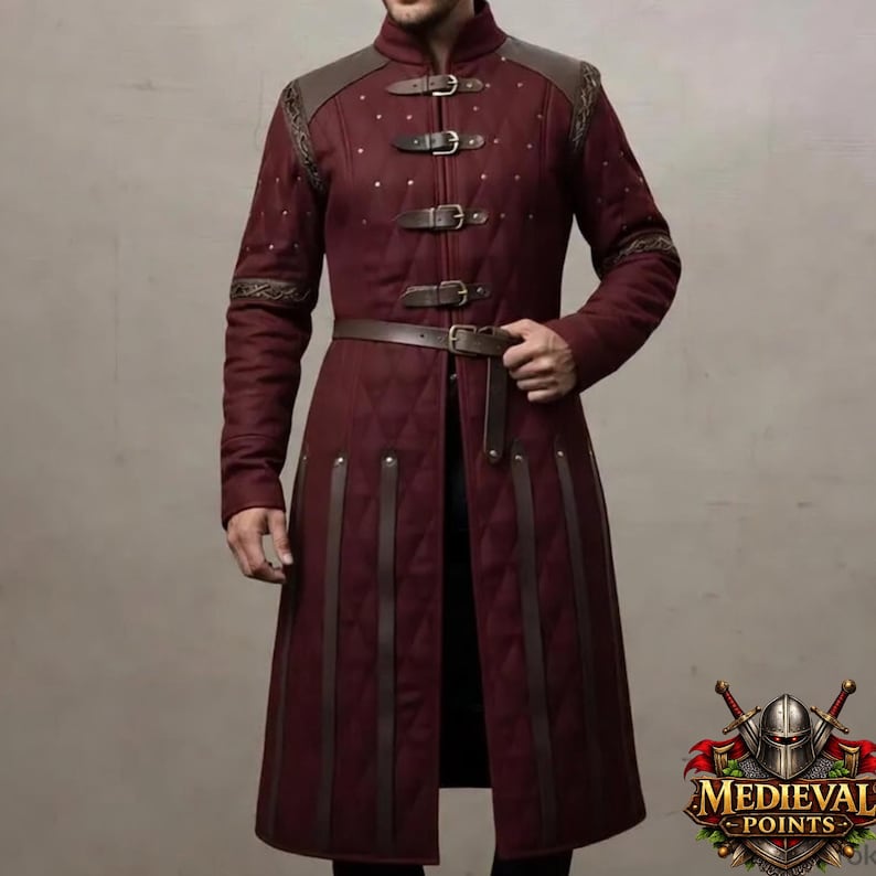 May include: A burgundy quilted coat with brown leather accents. The coat features a stand-up collar, shoulder patches, and a belt. It has three buckles on the chest and vertical leather straps down the front. The coat is part of the Medieval Points collection.