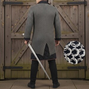 May include: A silver chainmail shirt with long sleeves and a split hem, worn over black pants and a quilted undergarment. A long silver sword is held at the side. The background is a wooden door.