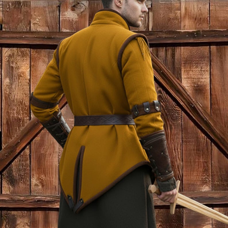 May include: Mustard-colored medieval tunic with brown leather accents. The tunic features a high collar, long sleeves, and a decorative belt. Brown leather arm guards are also visible. The tunic is worn over dark green pants. A wooden sword is held.