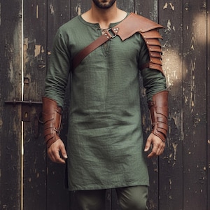 May include: Olive green tunic with long sleeves, paired with brown leather shoulder armor and arm bracers. The armor features layered plates and straps. The outfit is designed with a medieval or fantasy theme.