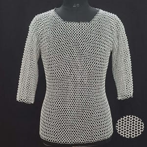 May include: A silver chainmail shirt with three-quarter sleeves. The shirt is displayed on a black mannequin. The chainmail is made of small, interlocking metal rings, creating a flexible, protective garment. A close-up of the chainmail is shown in the lower right corner.