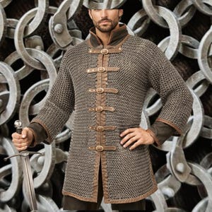 Puede incluir: Una cota de malla con detalles en cuero marrón y cuello alto. La camisa presenta correas de cuero con hebillas de latón en la parte delantera. Las mangas tienen puños de cuero marrón. Una espada se sostiene en la mano izquierda.
