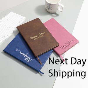 Peut inclure: Trois carnets personnalisés en bleu, marron et rose. Le carnet marron est estampillé "Daniela Garcia BOOK OF IDEAS". Le carnet rose porte l'inscription "Samuel Dennis Lawyer". Le carnet bleu porte le nom "Allyson".