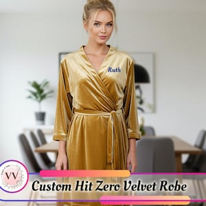 May include: A mustard-yellow velvet robe with a wrap-around style and a matching belt. The robe features long sleeves and the name "Ruth" embroidered in blue on the chest. The text "Custom Hit Zero Velvet Robe" is displayed at the bottom.