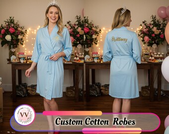 May include: A light blue cotton robe with a tie waist and three-quarter sleeves. The robe has a gold embroidered initial on the front and the name "Brittany" on the back. The text "Custom Cotton Robes" is displayed at the bottom of the image.