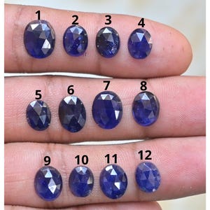May include: Twelve oval-cut, deep blue gemstones are displayed. Each gem has a unique faceted design, reflecting light internally. The gems are presented against a neutral backdrop, emphasising their colour and clarity. These gemstones are suitable for jewellery making, with each gem's dimensions in cm.