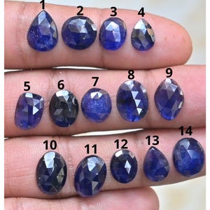 May include: Fourteen deep blue gemstones with various cuts, including oval, pear, and round shapes. The gems are displayed against a neutral background, highlighting their colour and clarity. Measurements are not available.