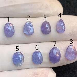 Könnte beinhalten: Acht facettierte, ovale und tropfenförmige Edelsteine in Lavendel- und Lilatönen werden gezeigt. Die Edelsteine sind mit 1 bis 8 nummeriert. Die Edelsteine liegen vor einem weißen Hintergrund.