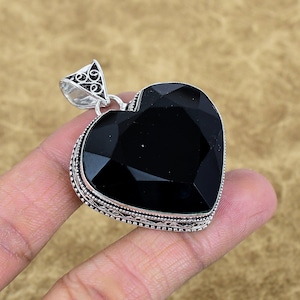 May include: A heart-shaped black gemstone pendant with a silver-colored bail. The gemstone has a faceted surface, and the pendant's edges are detailed with an ornate design. The pendant is held up by a silver-colored bail with a decorative pattern.