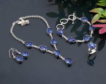 May include: A jewelry set featuring a necklace, bracelet, earrings, and ring. Each piece has a silver-colored metal setting and features a teardrop-shaped, deep blue gemstone. The necklace and bracelet have a chain design.