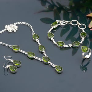 May include: A jewelry set featuring a necklace, earrings, bracelet, and ring. Each piece has a silver metal setting and features pear-shaped, olive-green gemstones. The necklace and bracelet have multiple gemstones, while the earrings and ring each have one.